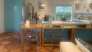 Una cocina moderna con un refrigerador azul, un área de comedor con sillas transparentes y una ventana que ofrece vistas de la vegetación exterior.