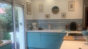 Una cocina con armarios azules, una encimera blanca y un salpicadero de azulejos. Se observan cuadros en la pared, una cafetera y un hervidor.