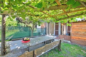 An outdoor wooden table with a red bowl of fruit under a pergola with green leaves. - Casa Arianna Garden (Laveno Mombello)