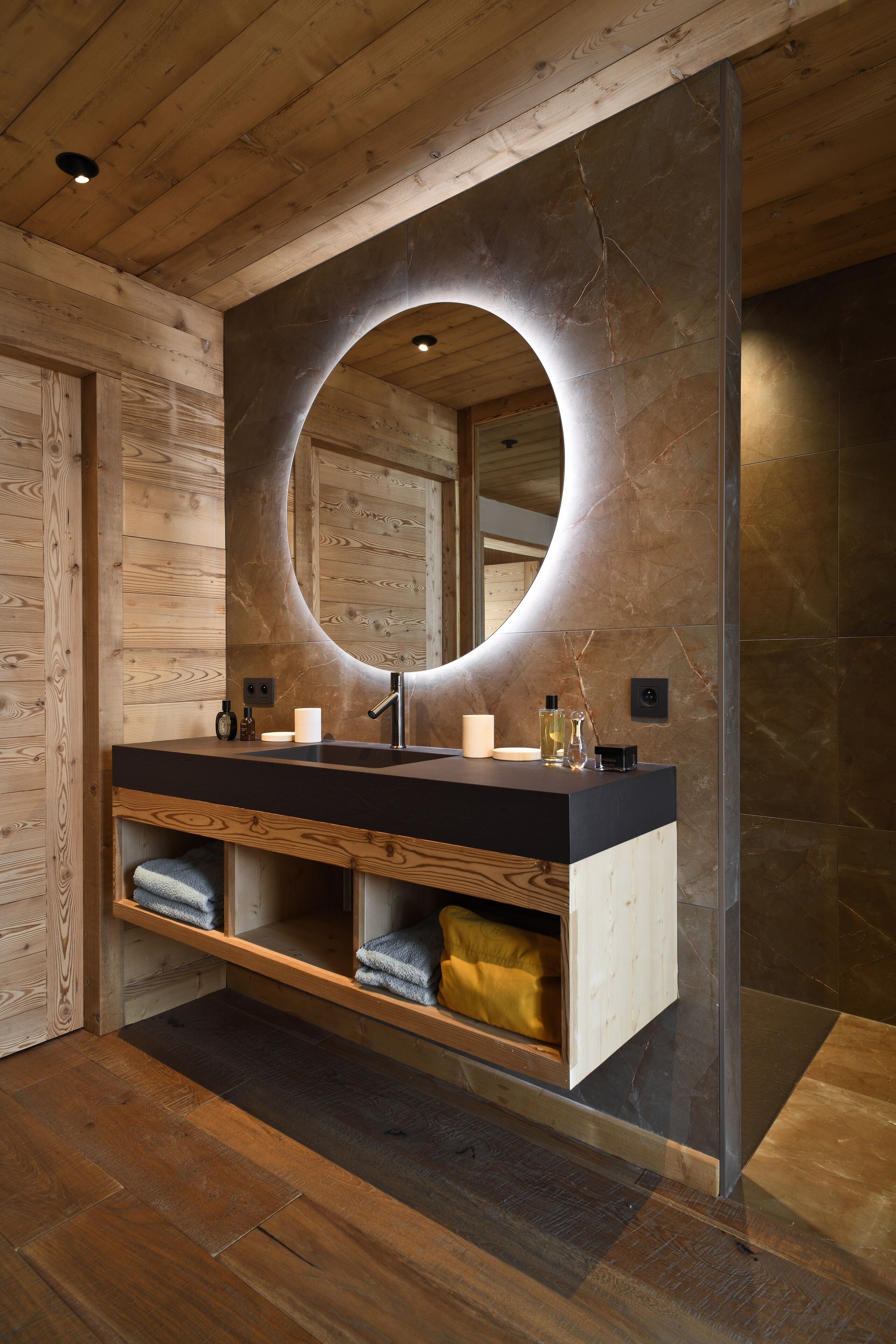 A modern bathroom with a wooden vanity, a large mirror, and a built-in towel rack.