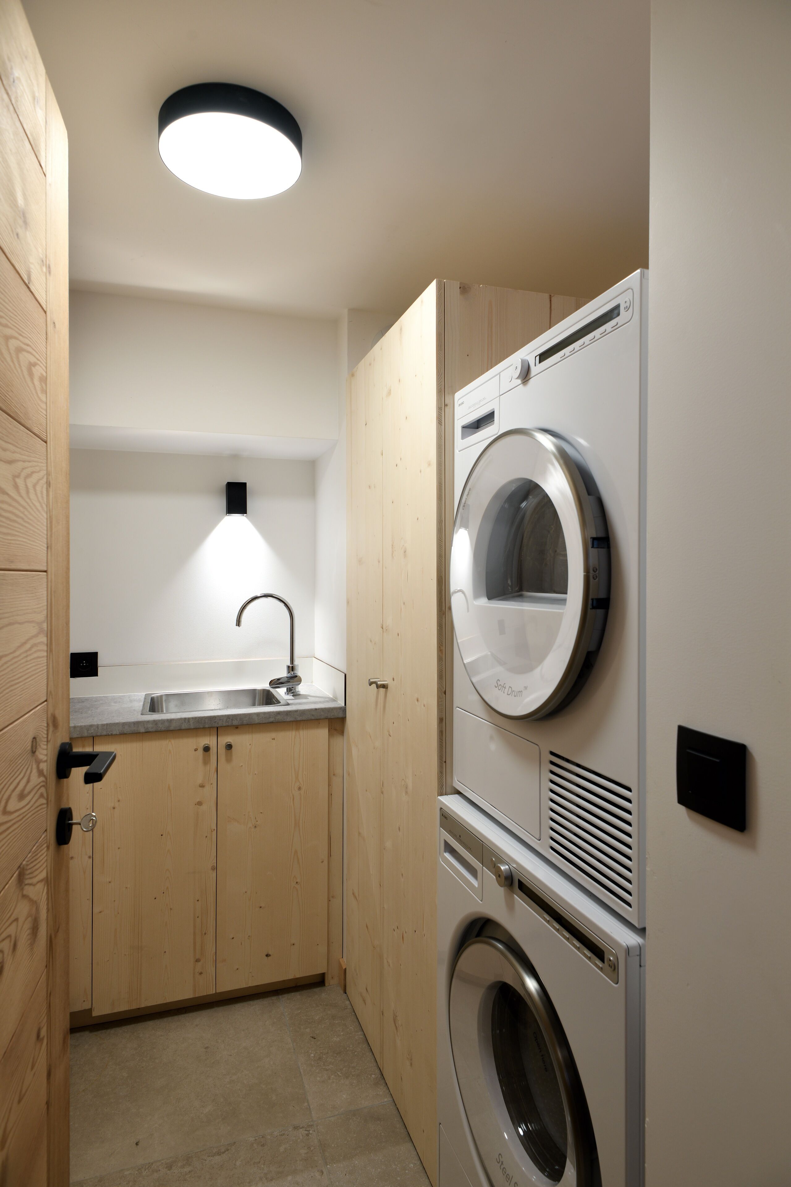 A compact laundry room with a built-in washer and dryer, a sink, and a wooden cabinet.