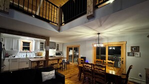 A spacious living area with a dining table, wooden flooring, and a black sofa with a 'welcome home' pillow. - Experience Lakeside Living with a Perfect Blend of Rustic Charm & Modern Luxury (Lunenburg)