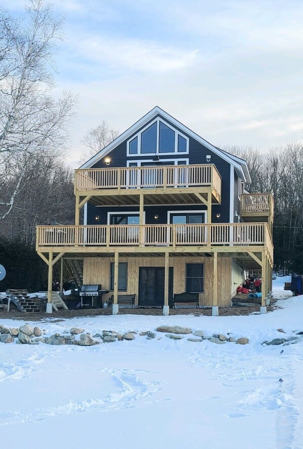 Une maison à deux étages avec un balcon à l’étage supérieur, un porche avant couvert et des fondations en pierre.