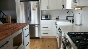 A modern kitchen with white cabinets, a stainless steel refrigerator, a microwave, and a gas stove. - Experience Lakeside Living with a Perfect Blend of Rustic Charm & Modern Luxury (Lunenburg)