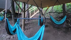 Hammocks suspended under a wooden structure, with a dirt ground and a wooden staircase in the background. - Tiny Treehouse Cabin | Bluff Woodlands #1 (Elba)