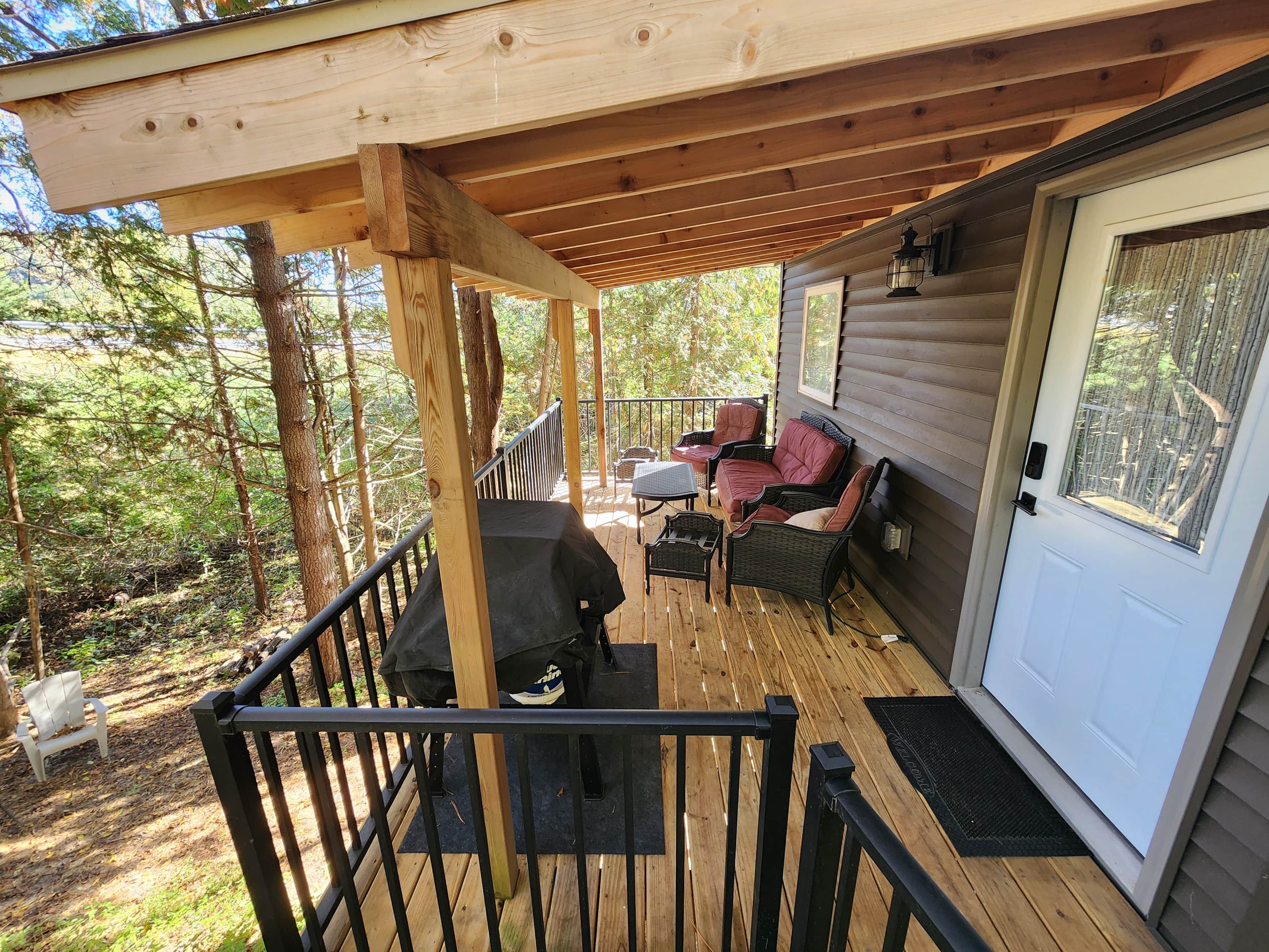 A covered deck with outdoor furniture, a grill, and a door leading to the interior.