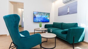 A teal armchair and sofa set, a small round table with two wine glasses, and a painting of a coastal scene. - Kipseli New Modern Cosy Apartments No 1 (Athens)