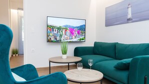 A modern living room with a teal sofa, a round coffee table, and a flat-screen TV displaying a colorful street scene. - Kipseli New Modern Cosy Apartments No 1 (Athens)