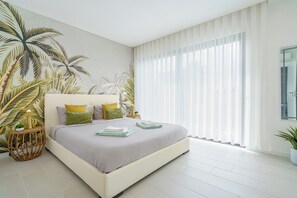 A modern bedroom with a large bed, a wall mural, and a large window with sheer curtains.