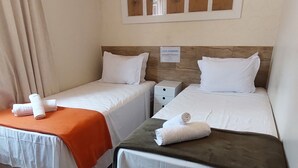 Een hotelkamer met twee bedden, elk voorzien van witte lakens en oranje dekens. Boven de bedden hangen prestatiekaders.
