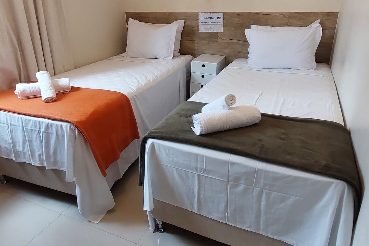 Habitación de hotel con dos camas, cada una con ropa blanca y mantas anaranjadas. Encima de las camas hay cuadros enmarcados en la pared.
