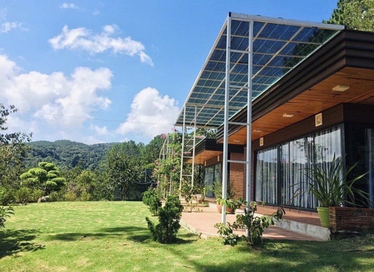 Una casa moderna con un amplio ventanal, rodeada de un césped cuidado y árboles.