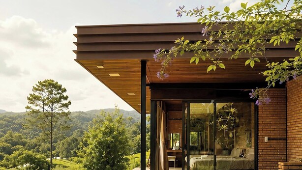 A modern house with a wooden deck, a glass door leading to a bedroom, and a view of the surrounding landscape. - Scent Bungalow (Xuan Huong - Da Lat)