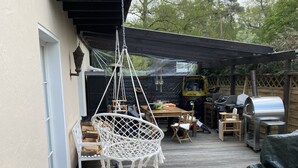 A patio area with a hanging chair, outdoor furniture, a grill, and potted plants. - Haus in Köln Thielenbruch (Köln)
