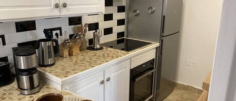 A compact kitchen with white cabinets, a microwave, a stainless steel refrigerator, and a coffee maker.
