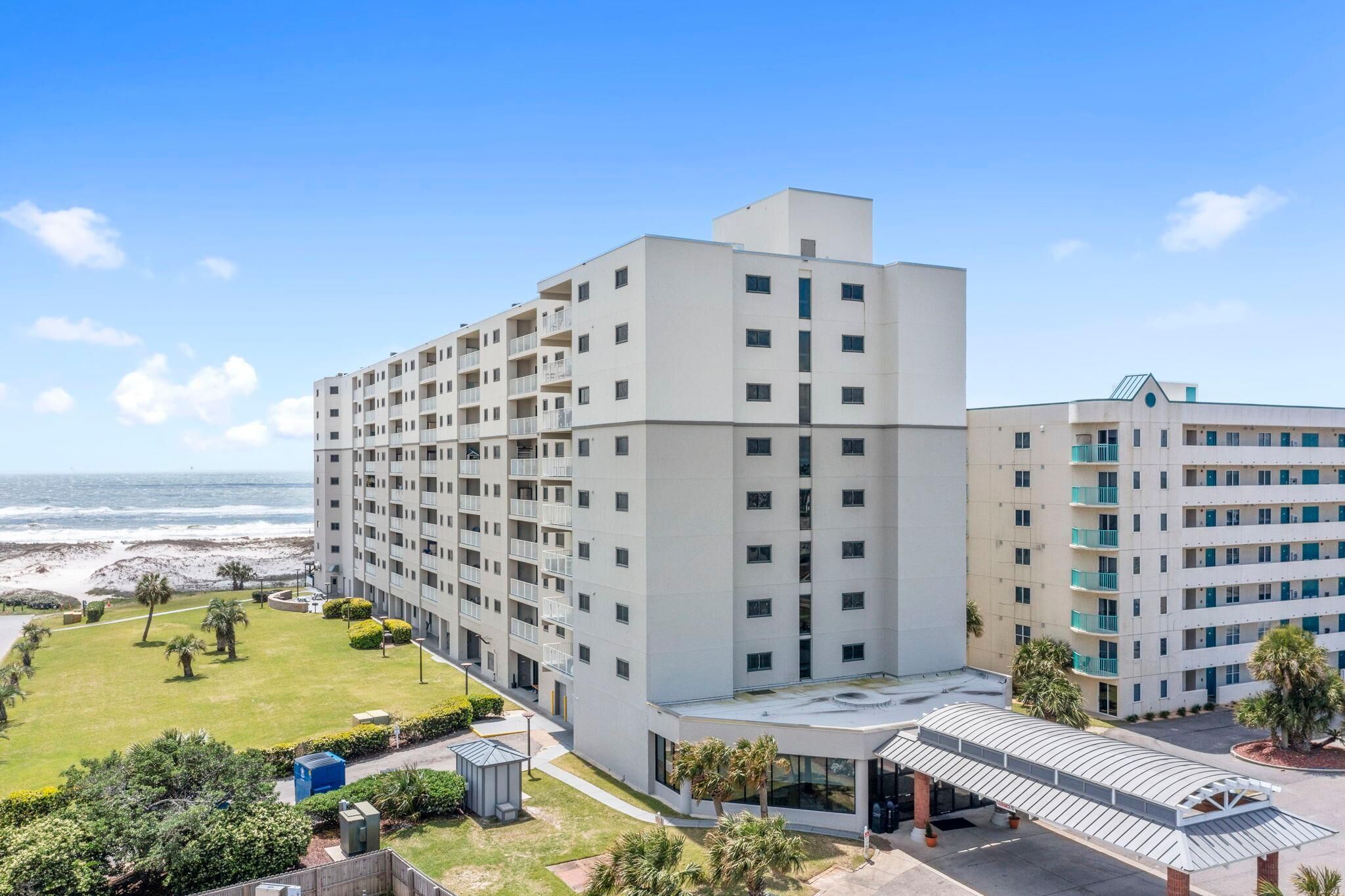 A multi-story hotel with a flat roof, a covered entrance, and a view of the beach.