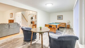Una sala de estar con mesa de billar, sofá y una escalera que lleva a otra habitación.