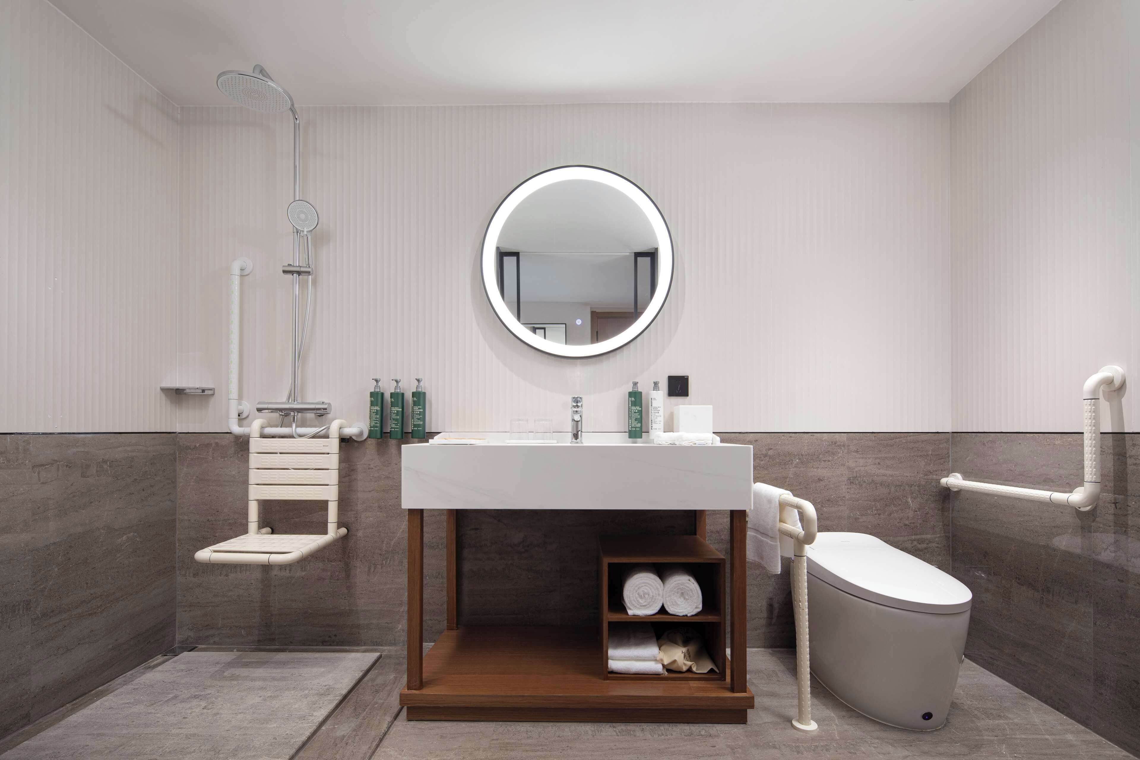 A modern bathroom with a white sink, a round mirror, a toilet, and a shower area.