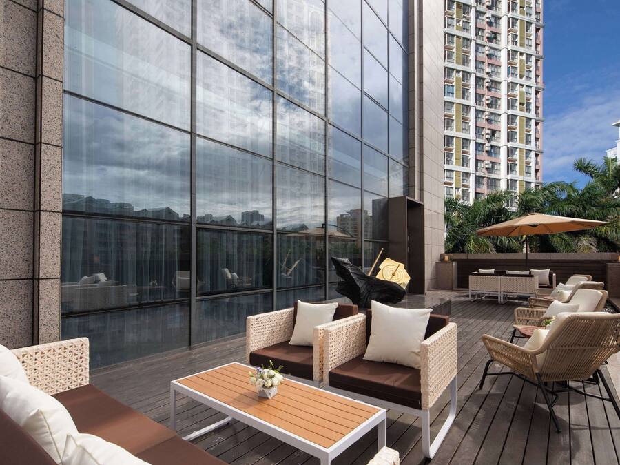 A modern outdoor lounge area with wicker furniture, a wooden coffee table, and a large umbrella.