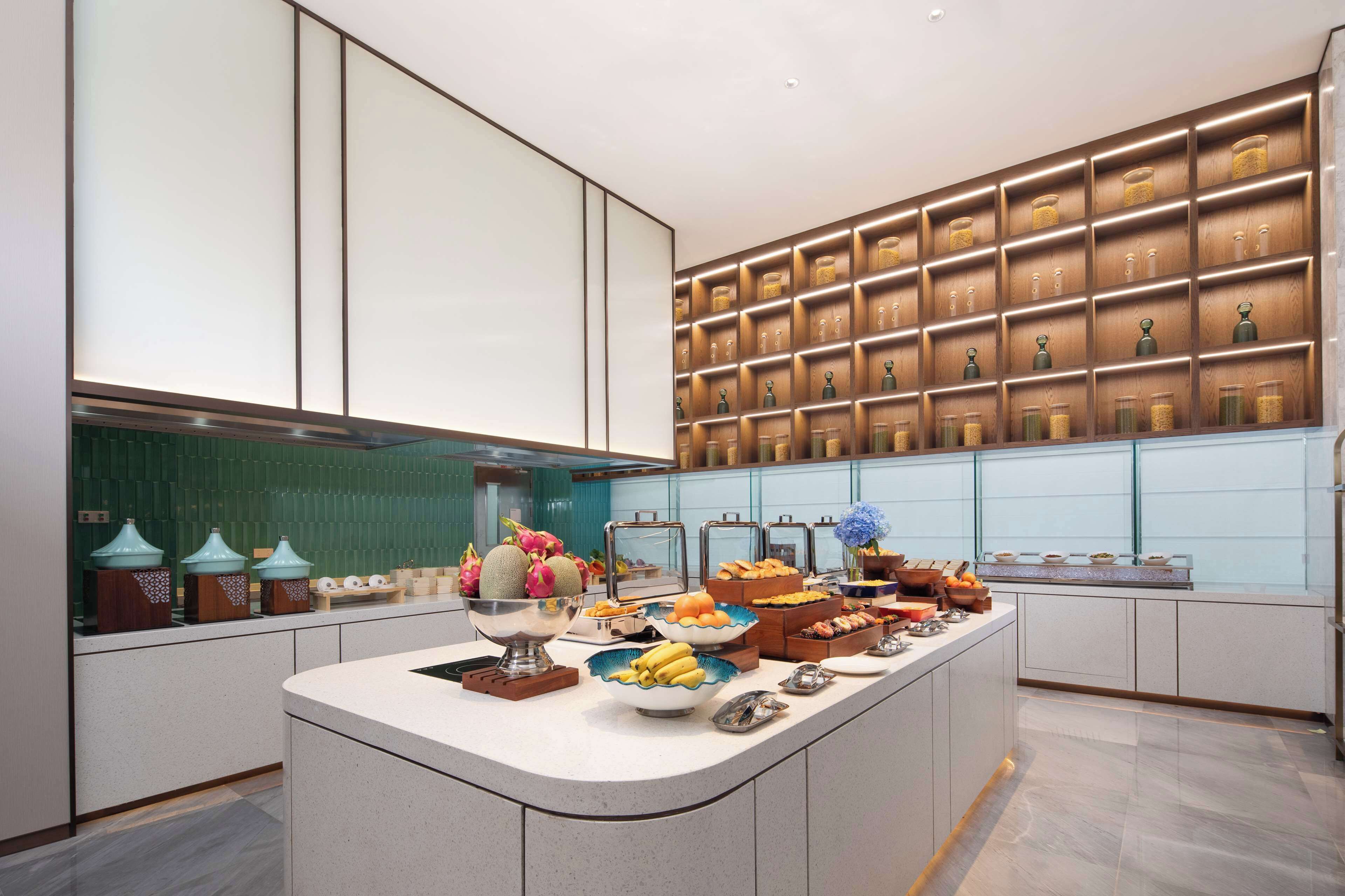 A modern kitchen with a central island, a variety of food items, and a wall of neatly arranged jars.