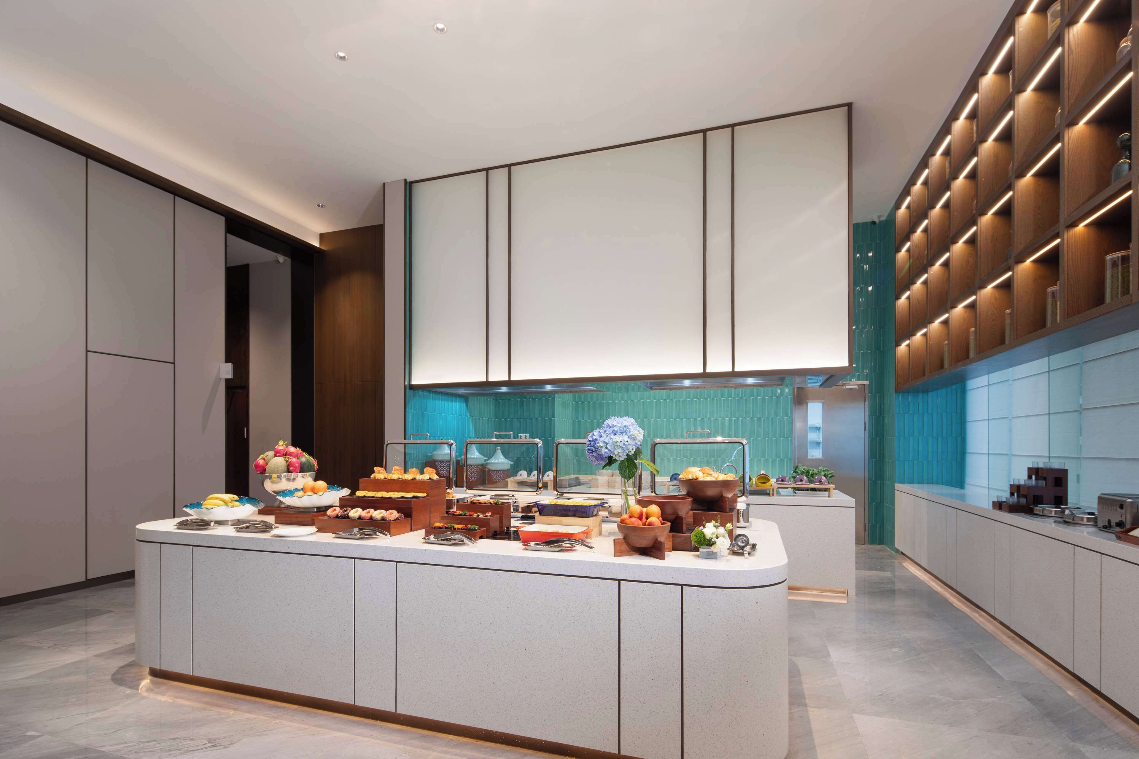 Una cocina moderna con una isla central, electrodomésticos integrados y un salpicadero en color verde azulado.