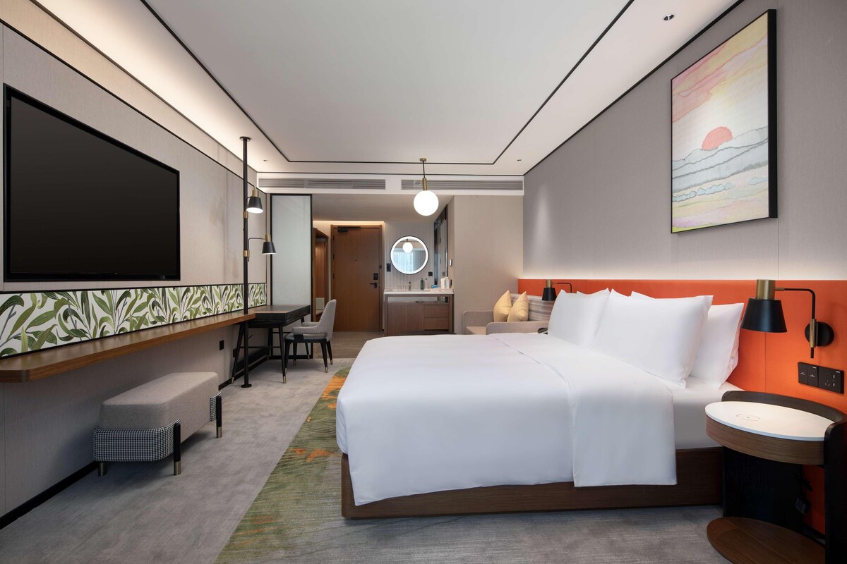 Une chambre d’hôtel moderne équipée d’un grand lit, d’un bureau, d’une chaise, d’une télévision et d’une salle de bain avec un miroir et un lavabo.