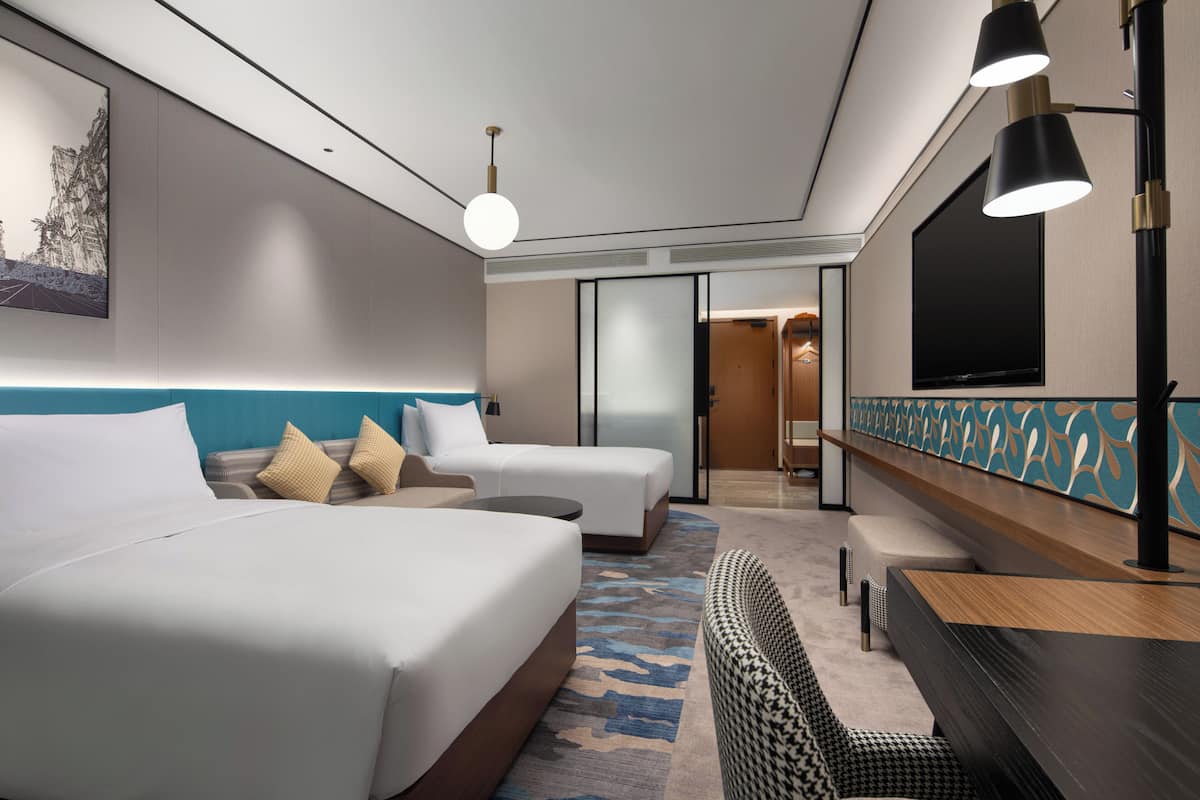 Een moderne hotelkamer met twee bedden, een zithoek, een televisie en een groot raam.