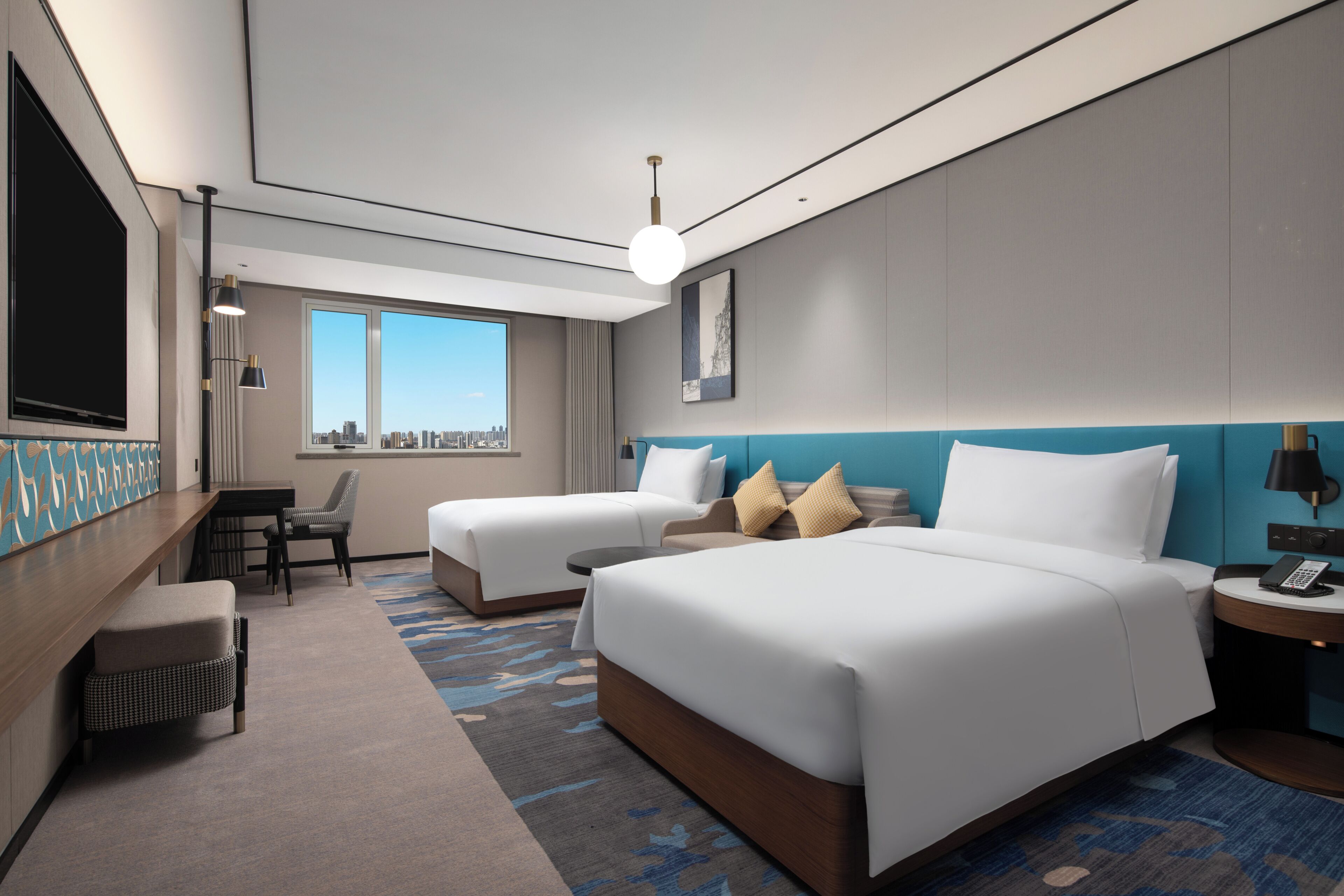 A modern hotel room with two beds, a desk, a chair, a TV, and a large window offering a city view.