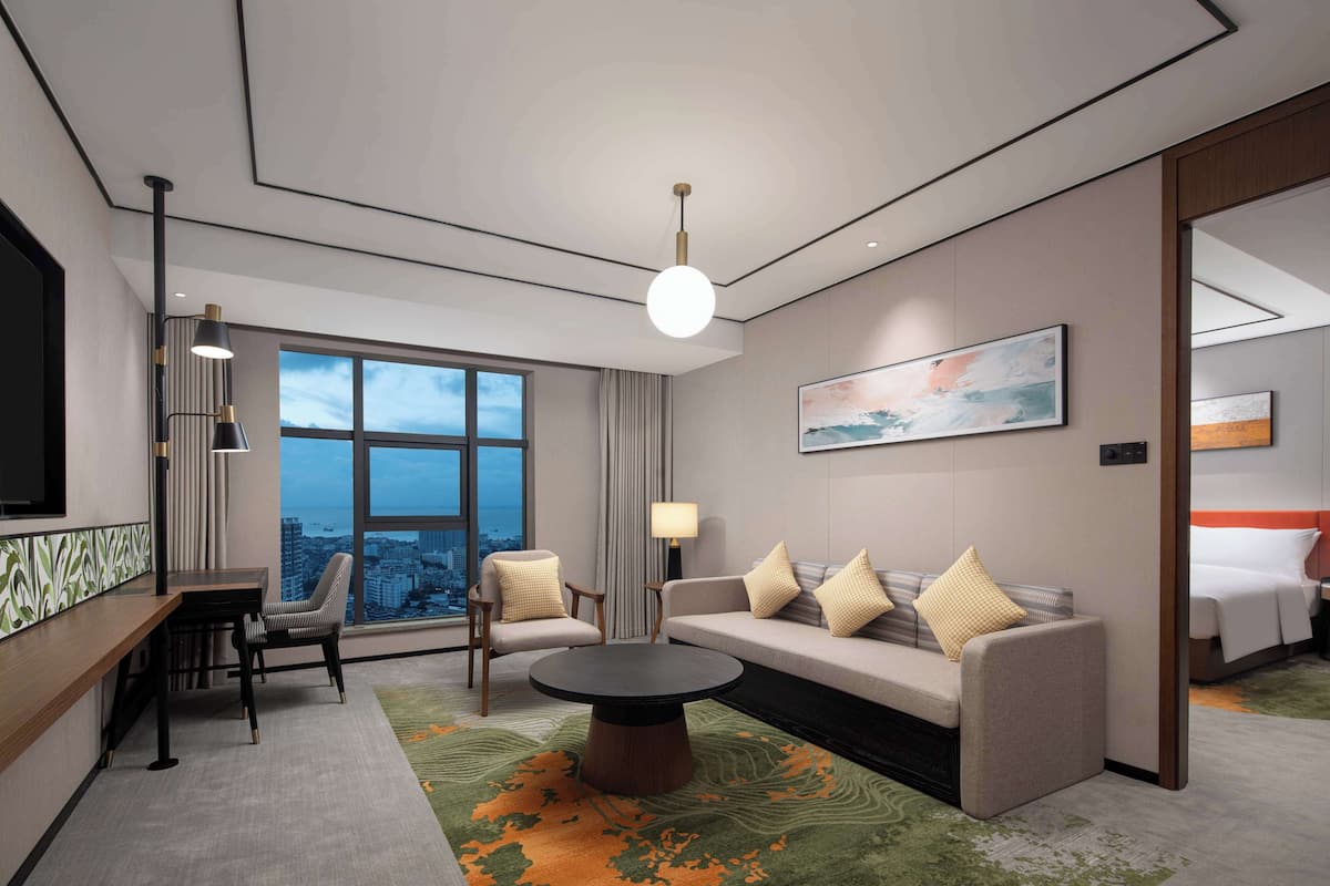 Een moderne hotelkamer met een groot raam, een bank, een salontafel en een bureau met een stoel.