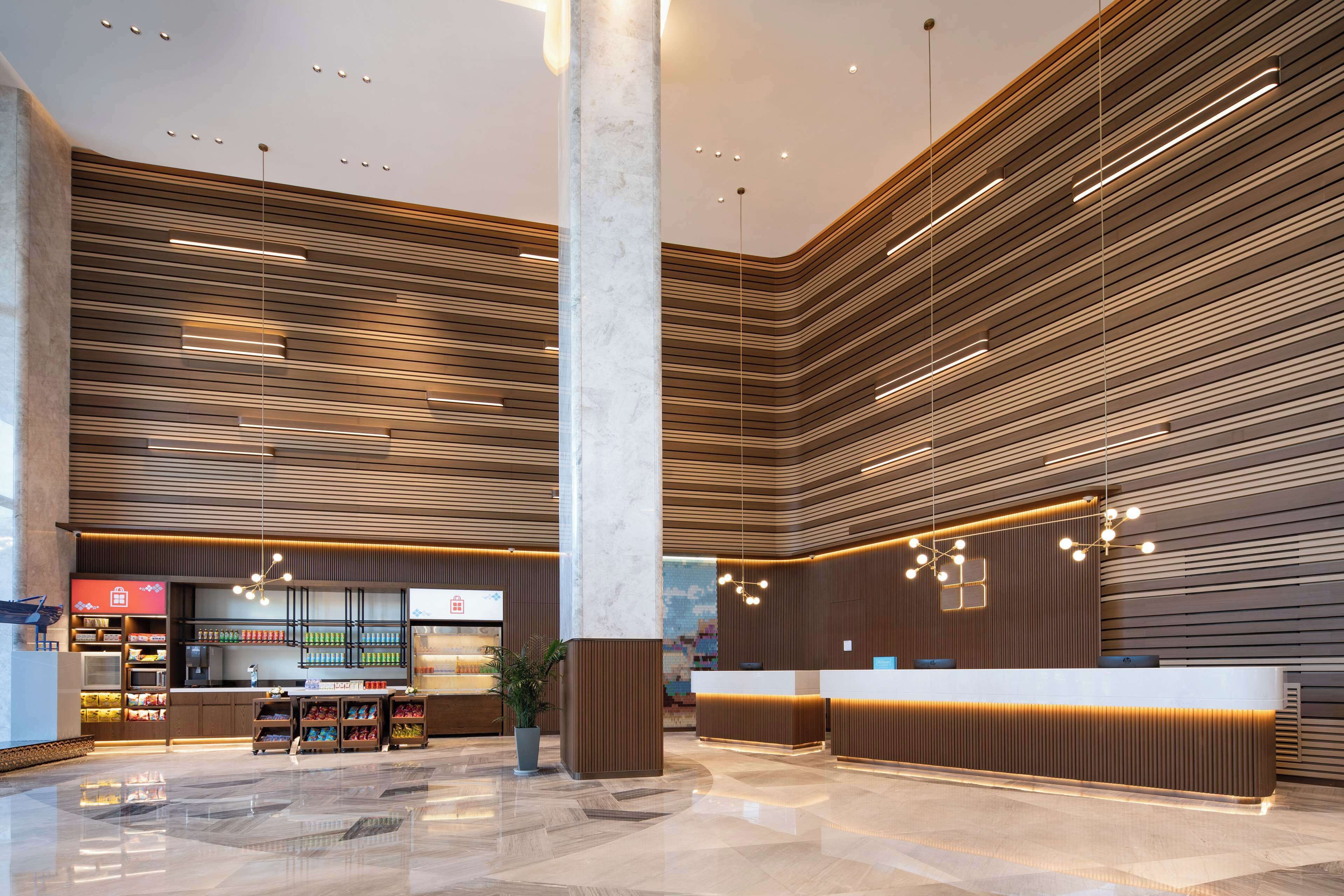 A modern hotel lobby with a reception desk, a large pillar, and a seating area with a plant.