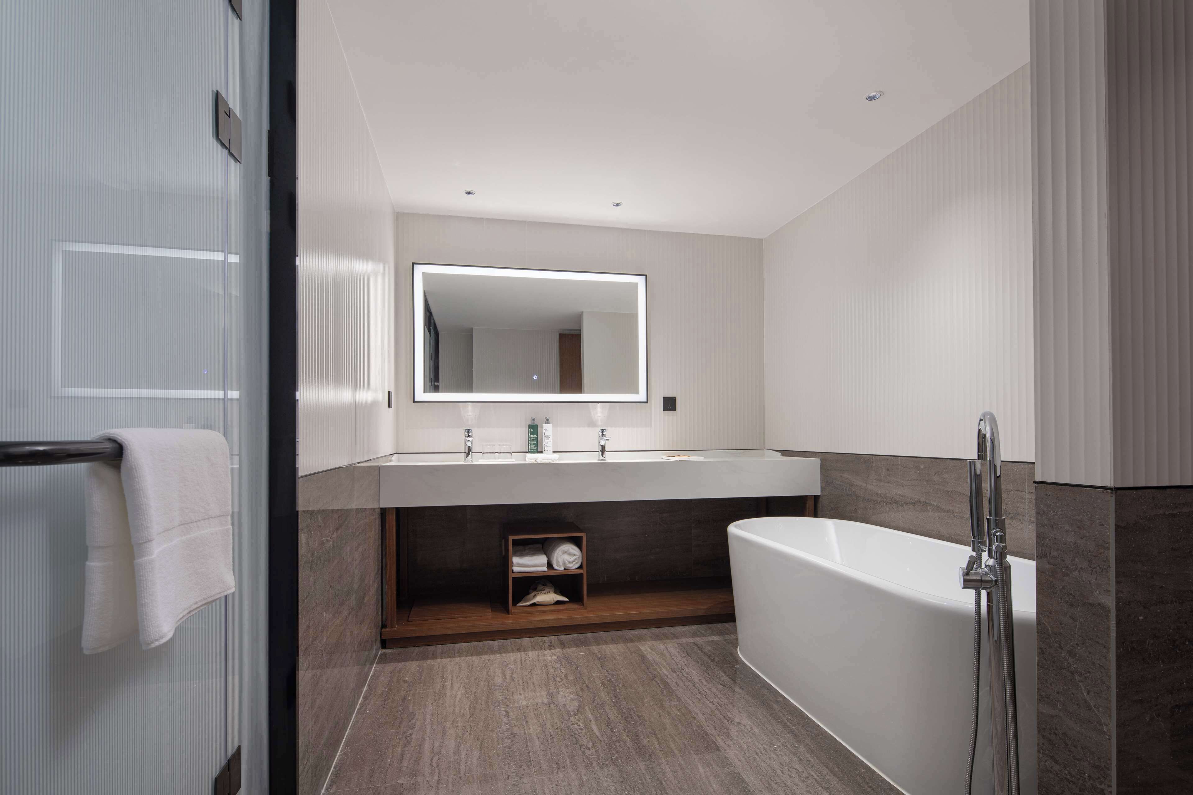 A modern bathroom with a large mirror, a bathtub, and a vanity with a shelf.