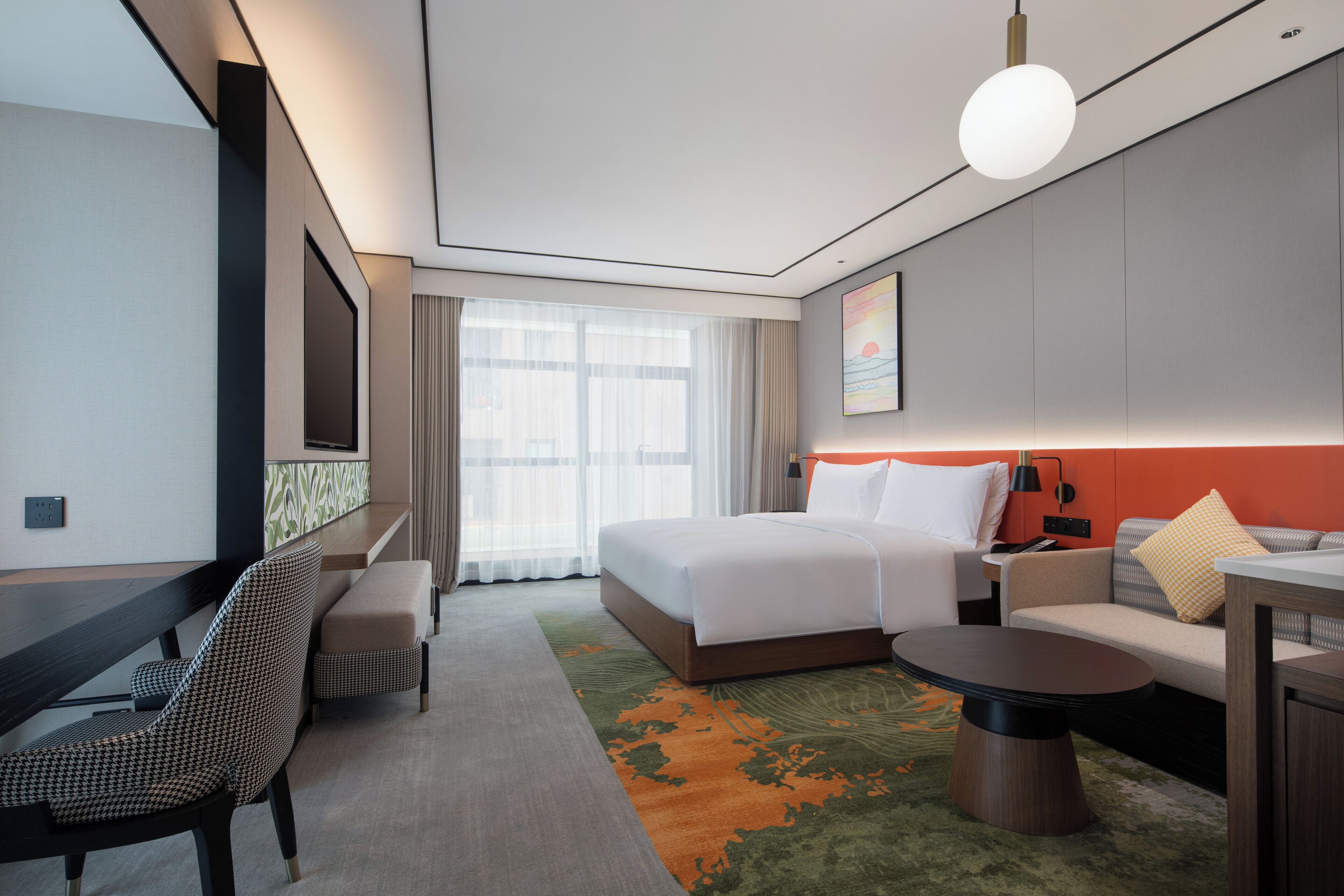 A modern hotel room with a bed, a sofa, a desk, and a chair.