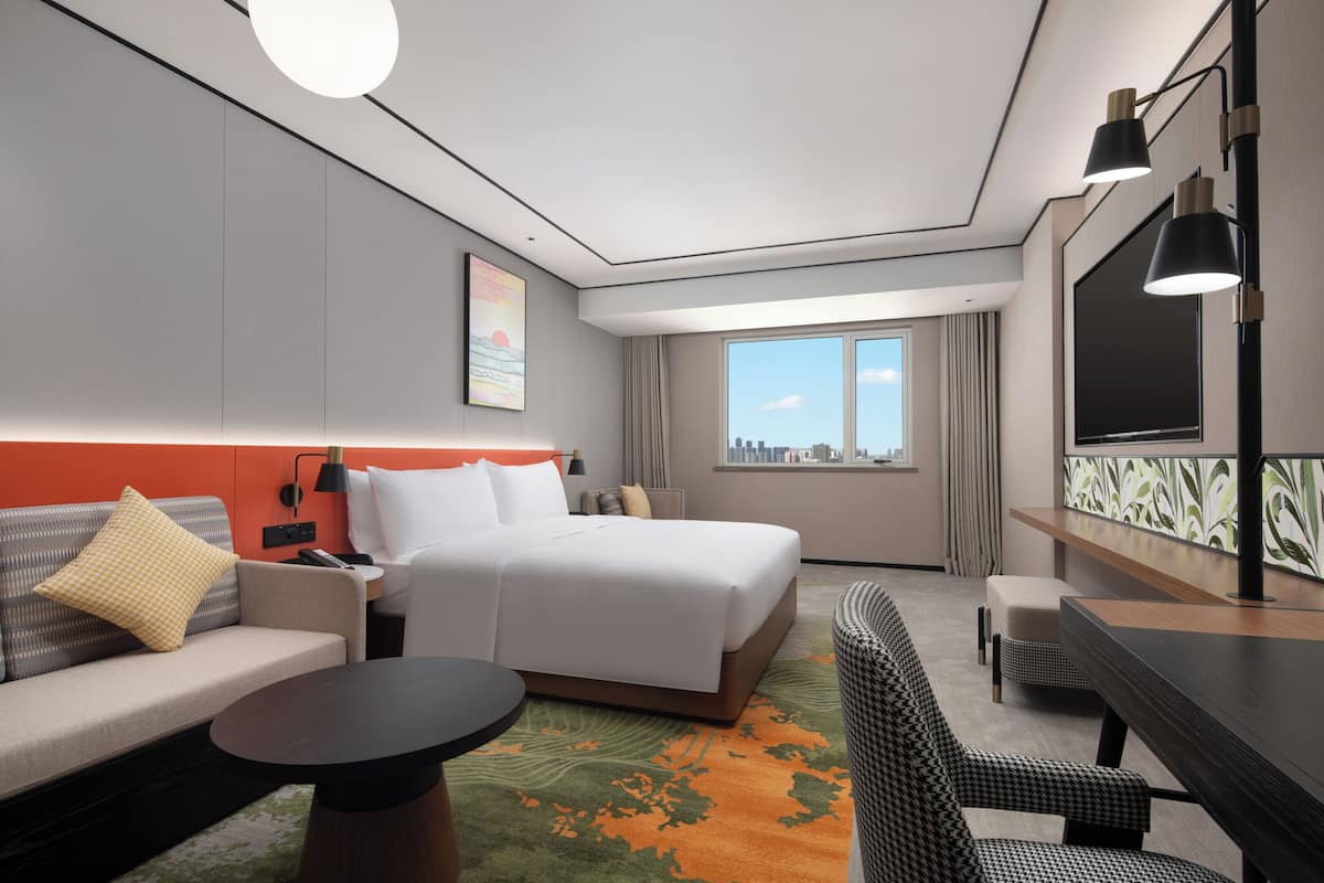Een moderne hotelkamer met een bed, een bank, een fauteuil, een bureau en een groot raam.