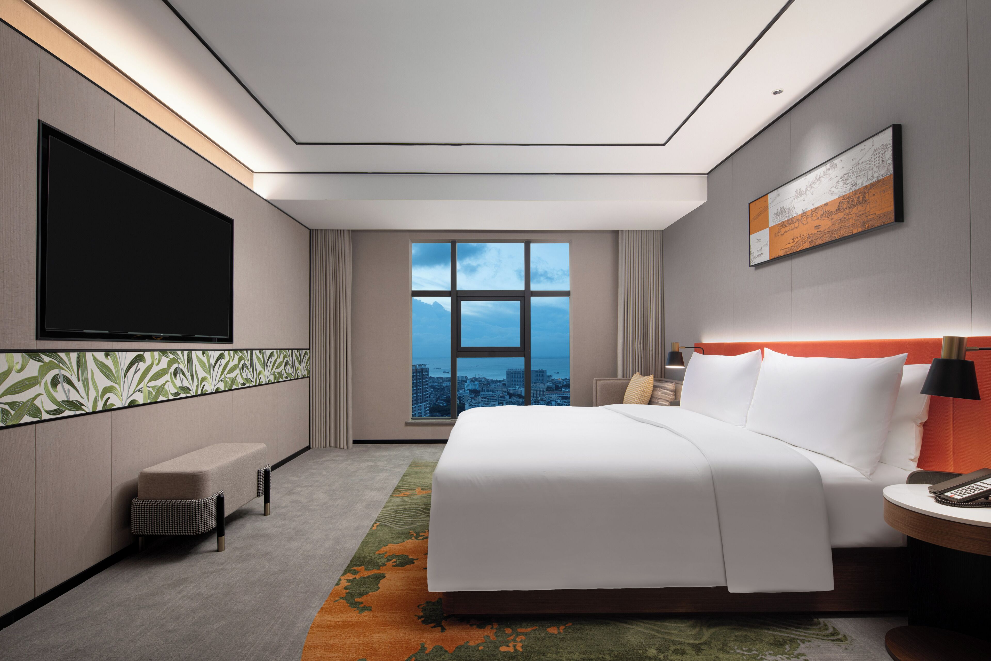 A modern hotel room with a large bed, a flat-screen TV, a city view, and a small seating area.