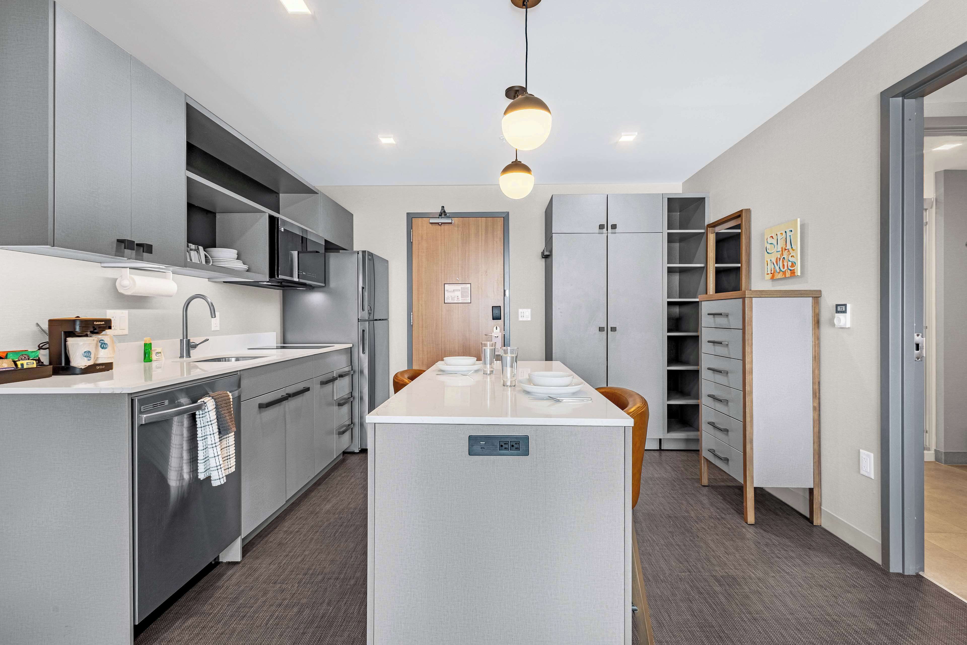 A modern kitchen with grey cabinetry, a central island, and a hanging light fixture.