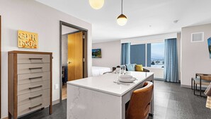 A hotel room with a marble island, a wooden dresser, a bed with a view, and a dining area with a view.