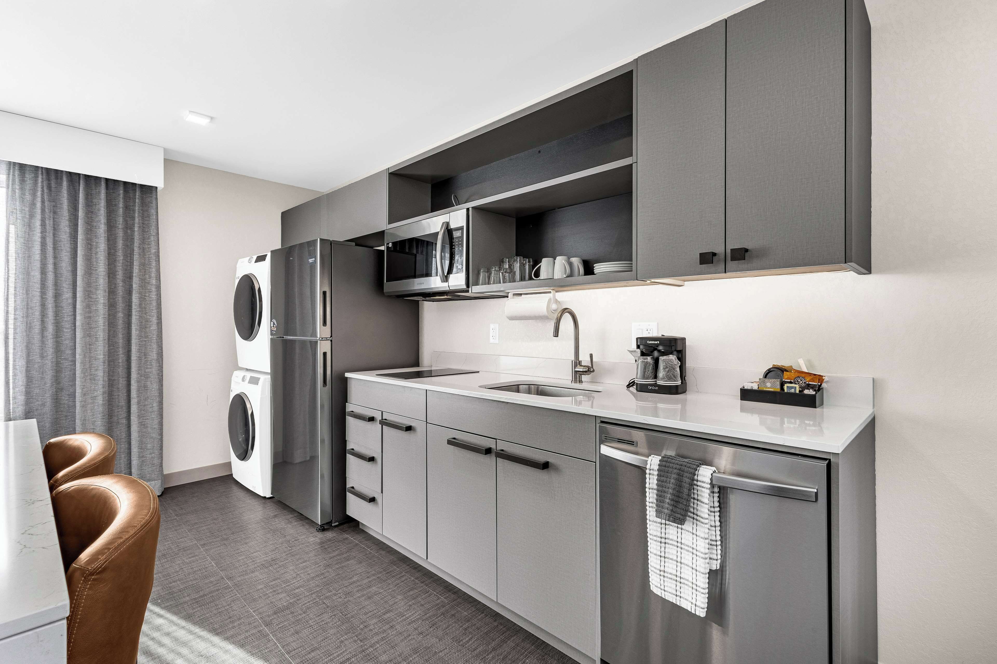 A modern kitchen with stainless steel appliances, grey cabinetry, and a built-in dishwasher.