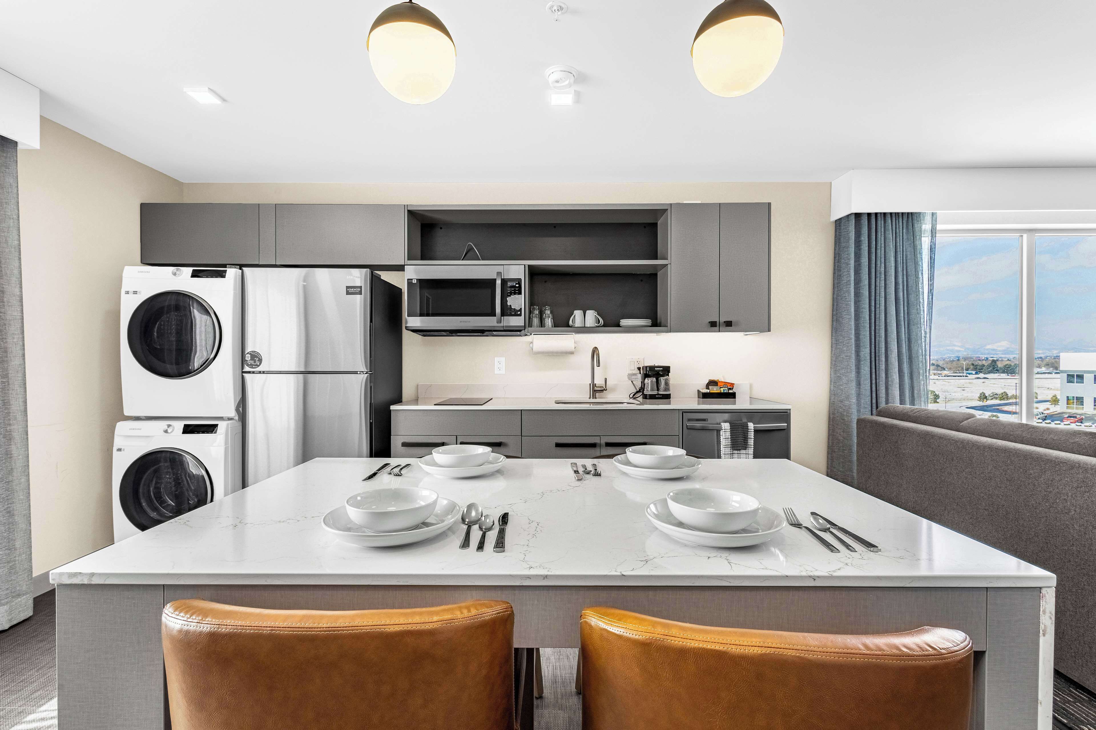 A modern kitchen with built-in appliances, a marble countertop, and a dining area with two chairs.