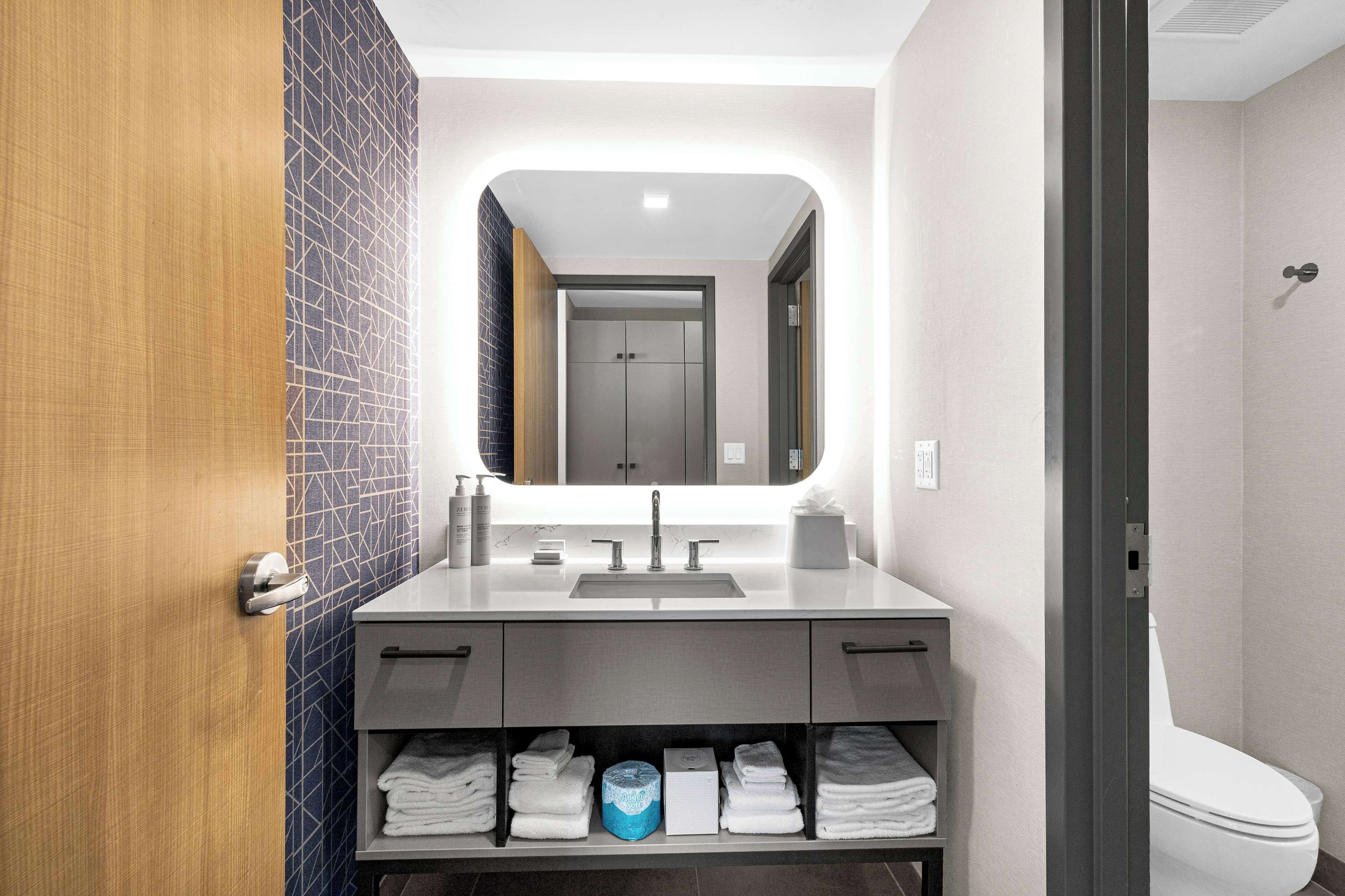 A modern bathroom with a large mirror, a sink, and a toilet.