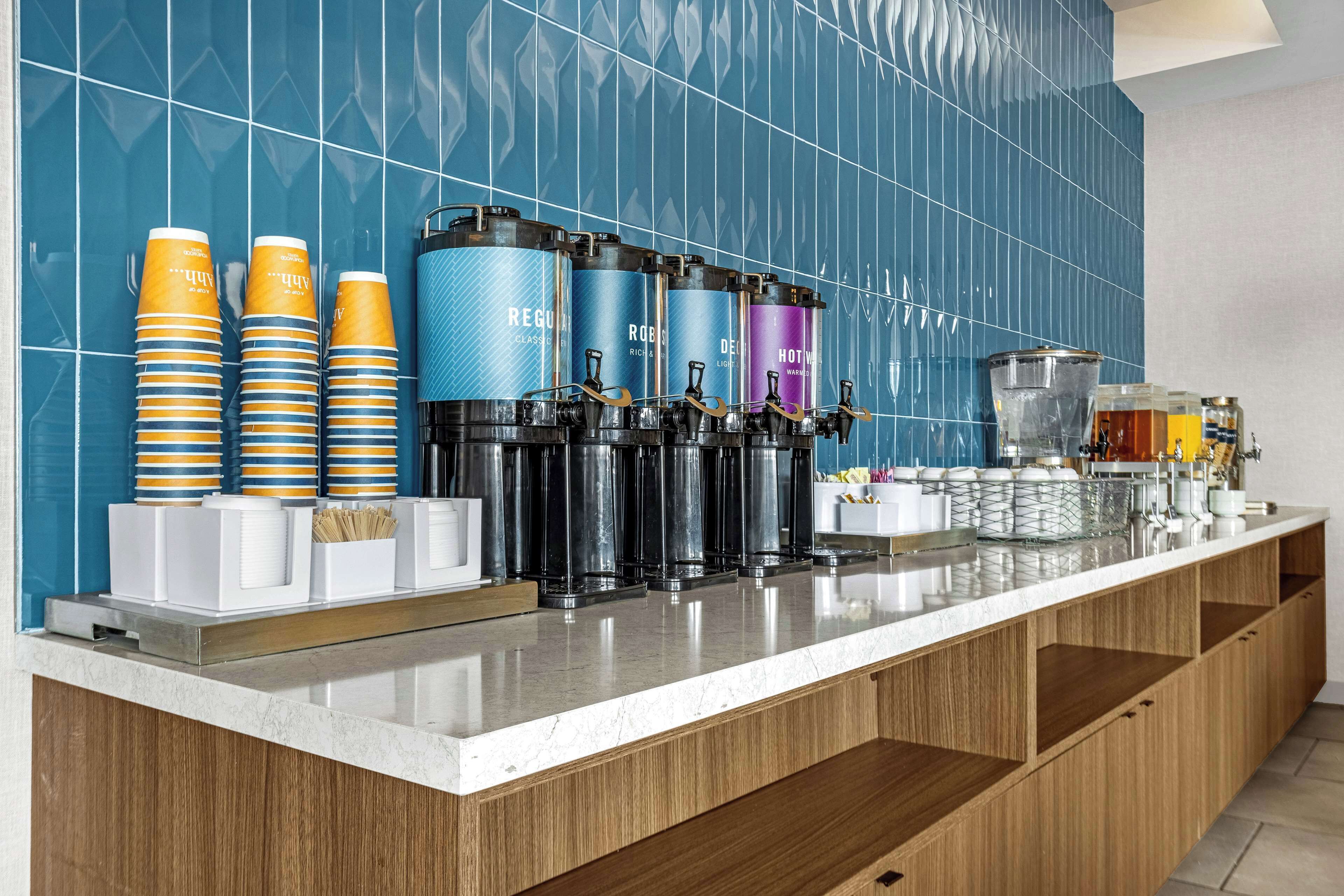 Een hotel receptie met een balie waarop koffieautomaten, papieren bekers en een koffieapparaat staan.