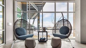 A modern interior with two hanging chairs, a small table with books, and a view of the outside through large windows.