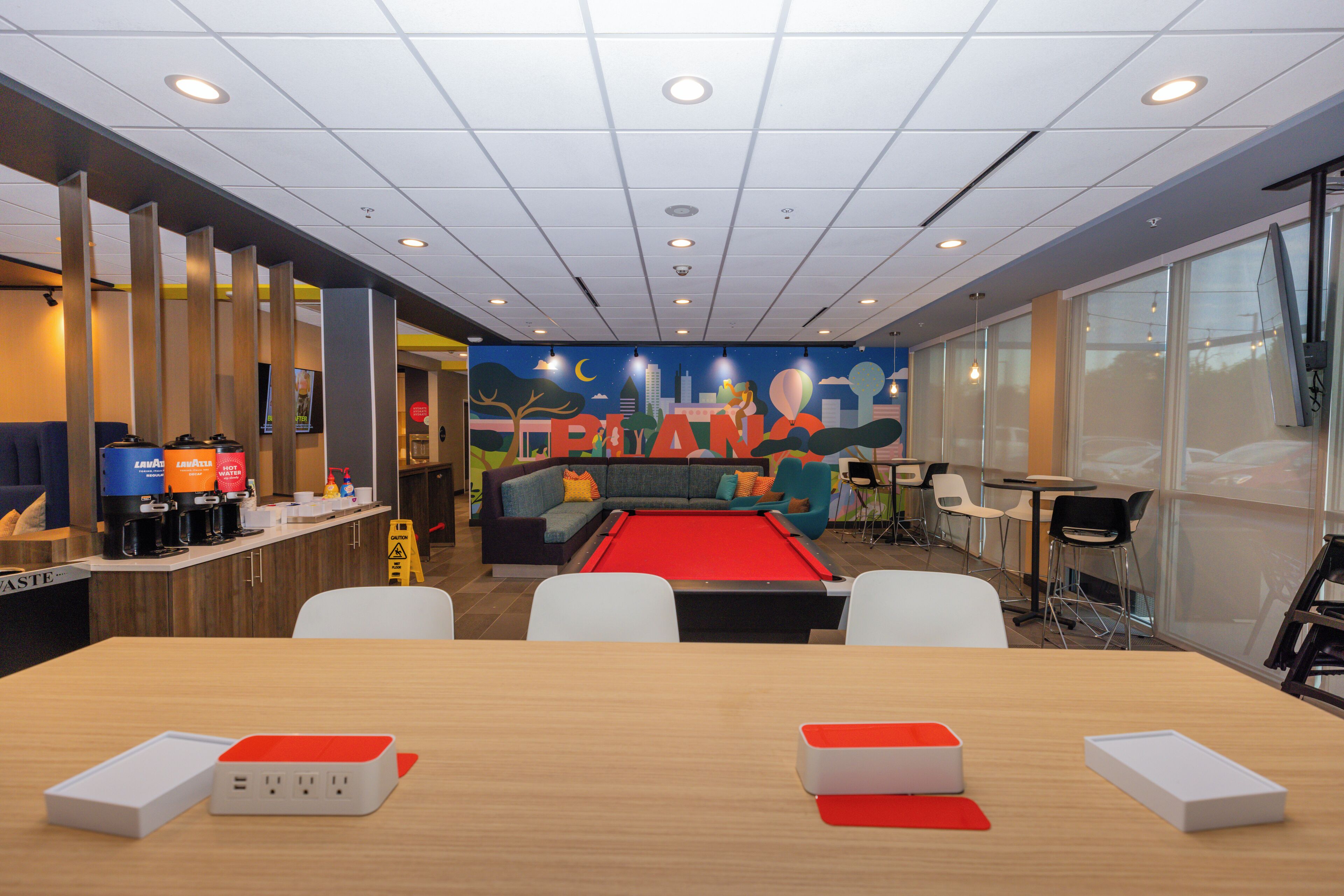 A modern lounge area with a pool table, comfortable seating, and a cityscape mural on the wall.
