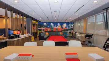 A modern lounge area with a pool table, comfortable seating, and a cityscape mural on the wall.