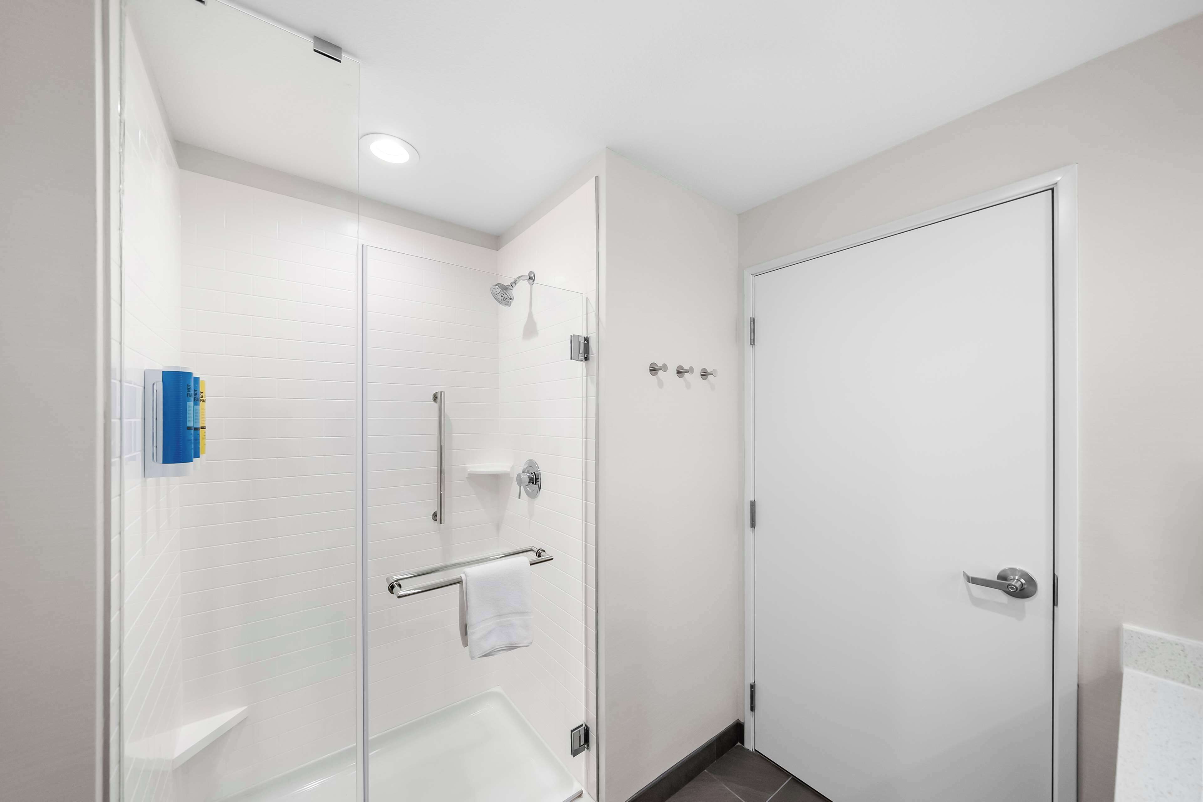 Une salle de bain moderne avec une douche à l’italienne en verre, une baignoire blanche et une porte blanche.