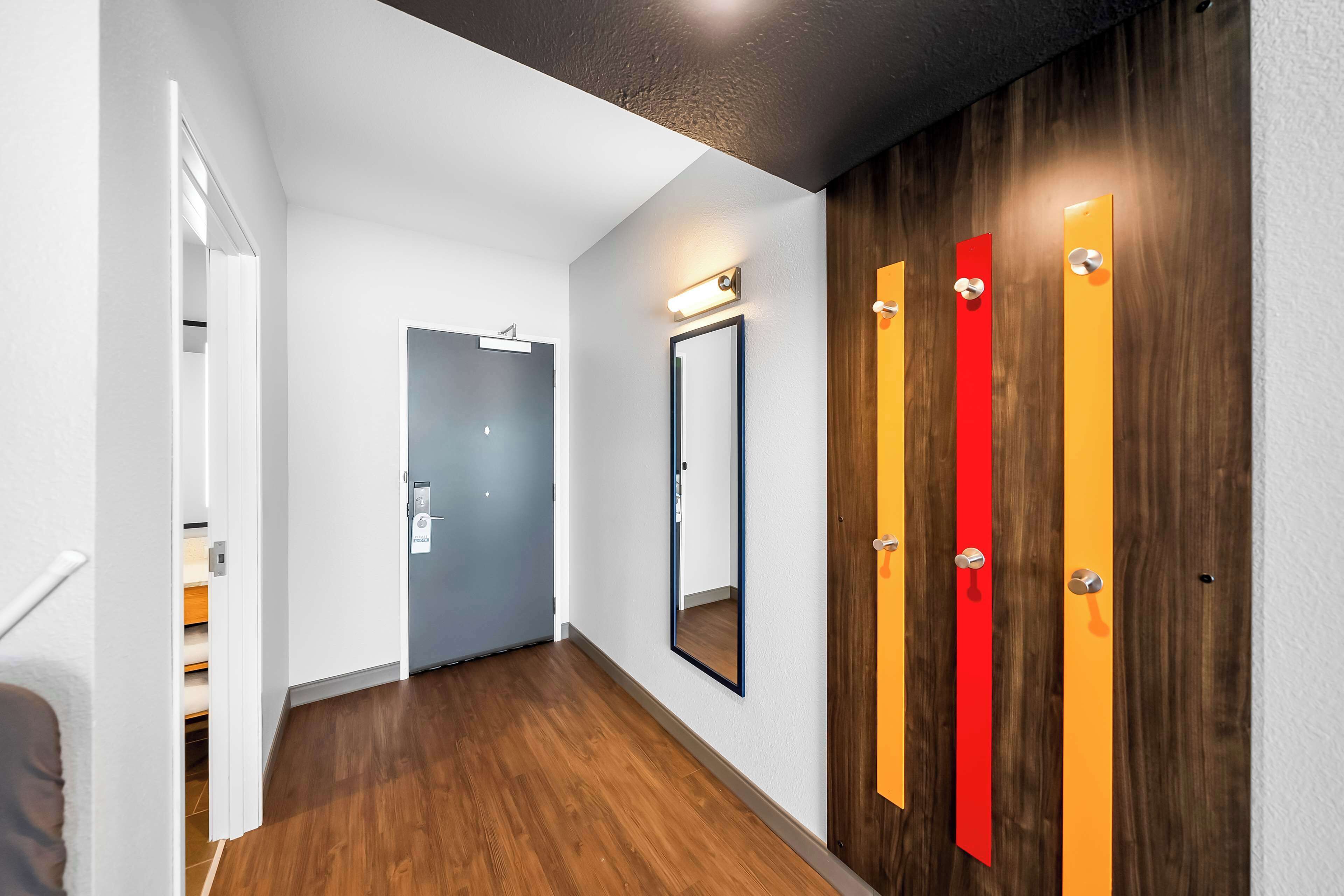 A hallway with wooden flooring, a white wall, and a door with vertical stripes.