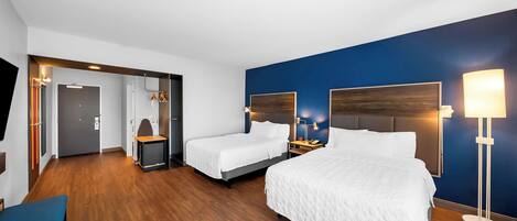 Une chambre d’hôtel avec deux lits, un bureau, une chaise et une lampe.