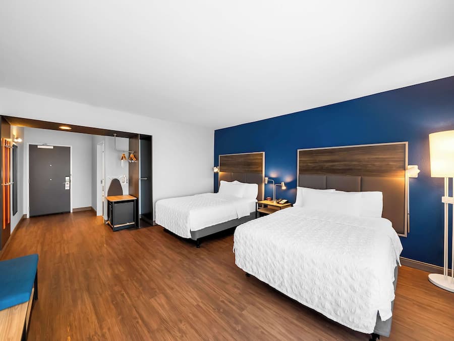 Habitación de hotel con dos camas, un escritorio, una silla y una lámpara.