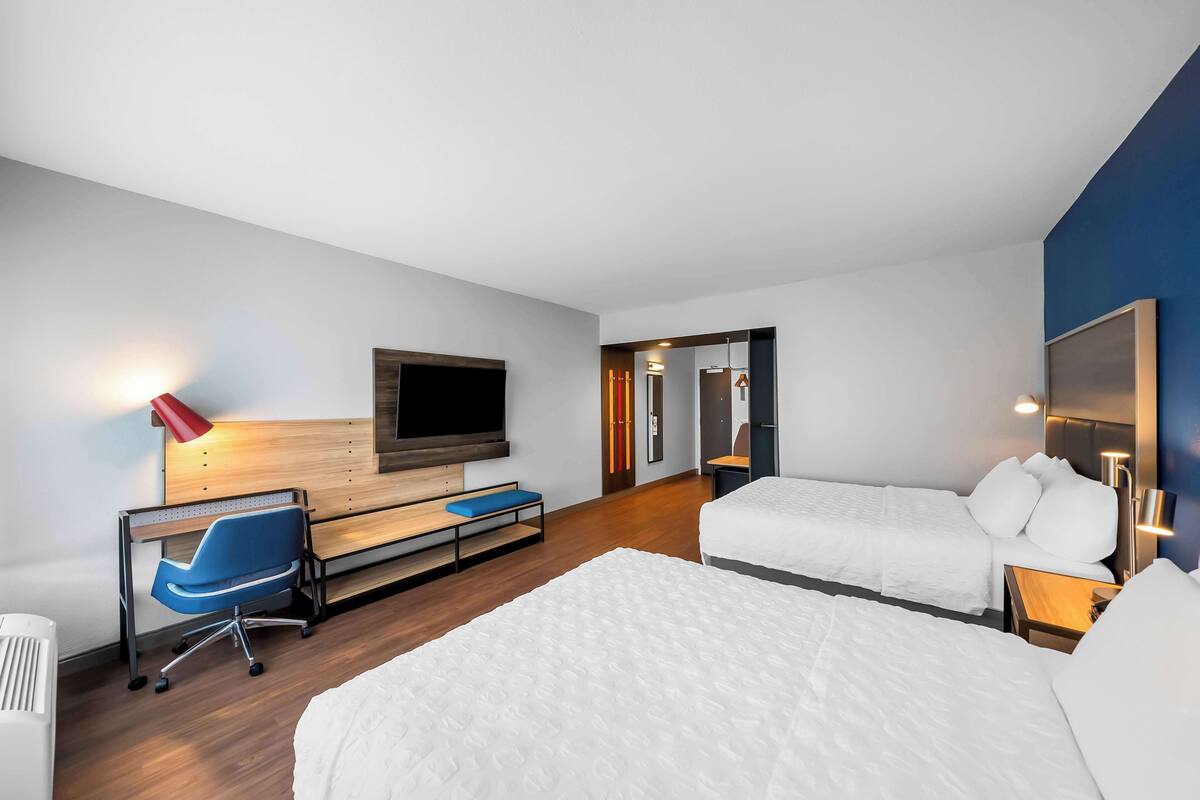 A modern hotel room with a large bed, a desk with a chair, a television, and a red lamp.