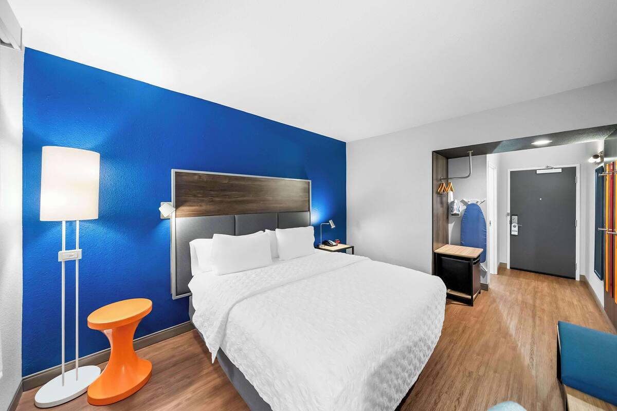 A hotel room with a large bed, a bedside table, a lamp, and a blue accent wall.