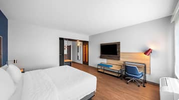Quarto de hotel moderno com uma cama grande, uma escrivaninha com cadeira, uma TV e um abajur vermelho.